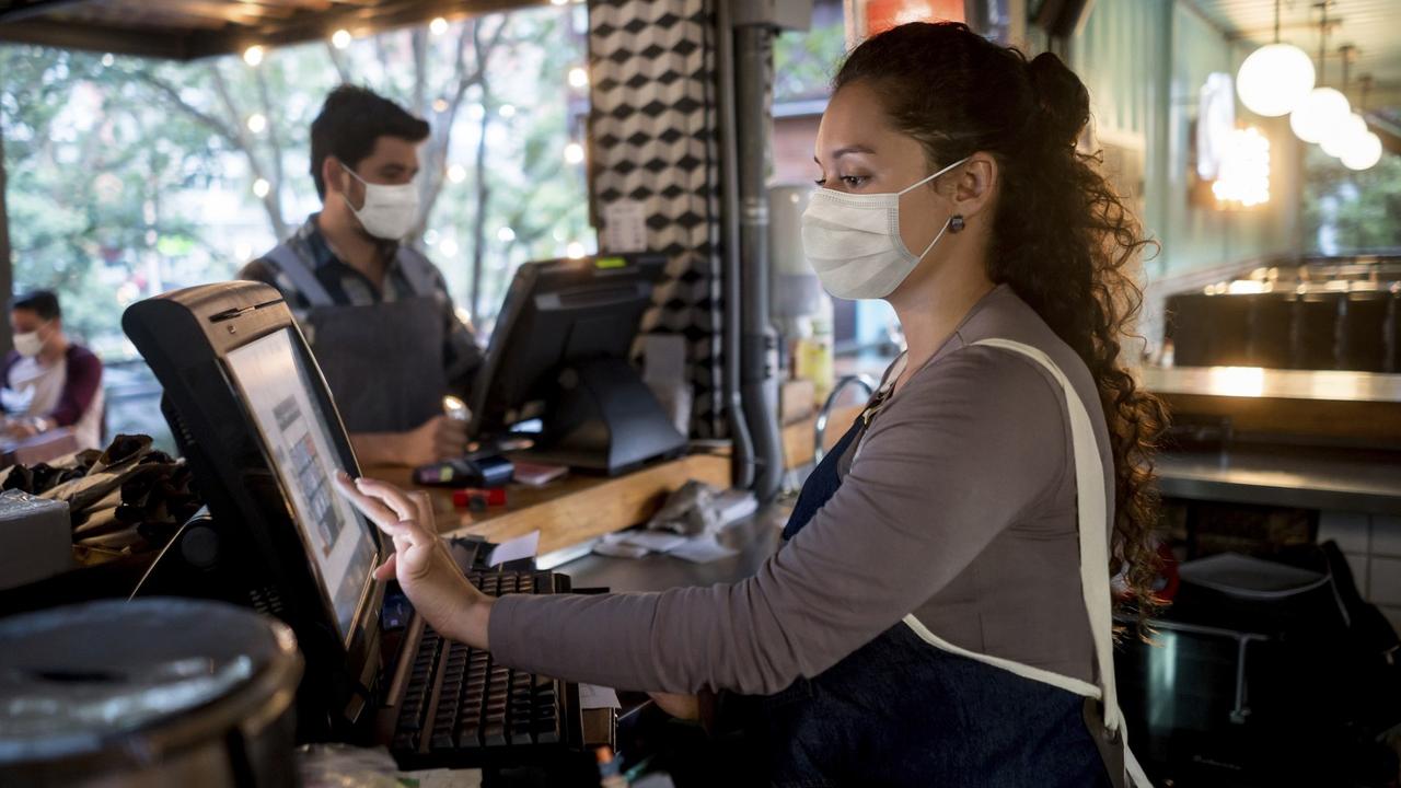 Woman working at the cashier at a restaurant wearing a facemask stock photo