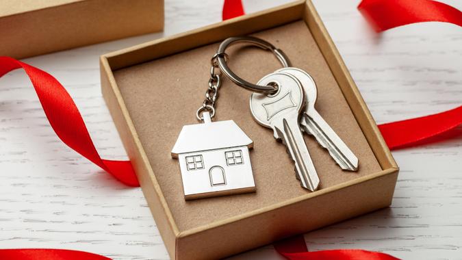 Keychain house and keys with red ribbon and gift box on white wooden background.