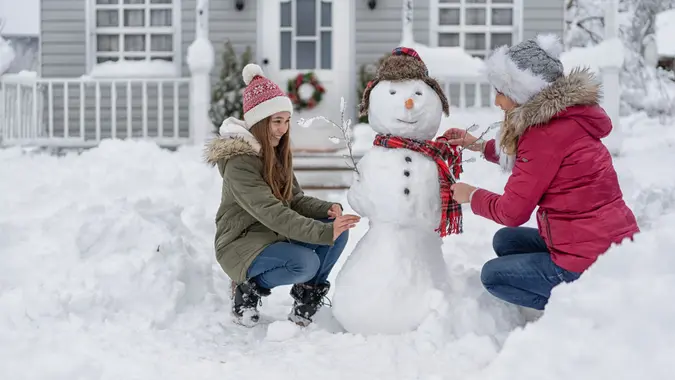 Mother and daughter making a snowman in front of the house.