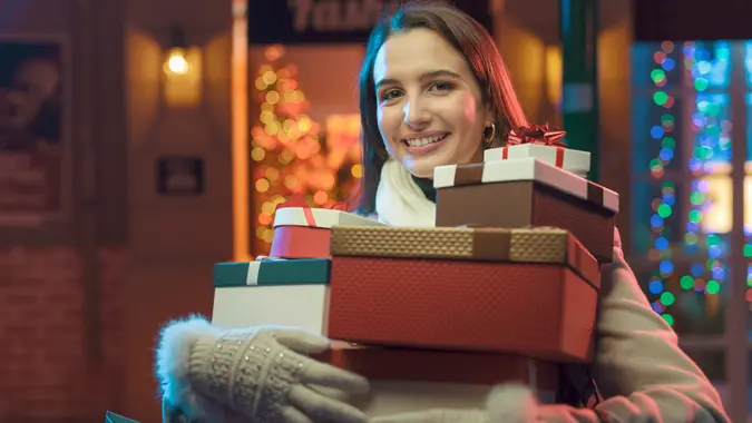 Happy woman doing Christmas shopping in the city street, she is holding a lot of gifts and smiling.