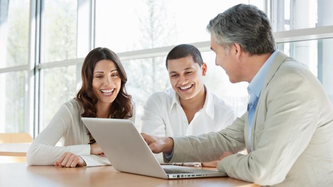 Mature financial consultant advising a happy young couple while using a laptop.
