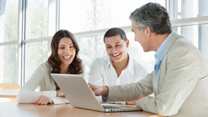 Mature financial consultant advising a happy young couple while using a laptop.