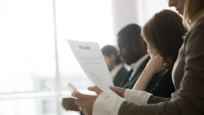 Multiracial business people waiting in queue preparing for job interview concept, diverse unemployed vacancy applicants holding reading cvs getting ready, human resources concept, focus on resume.