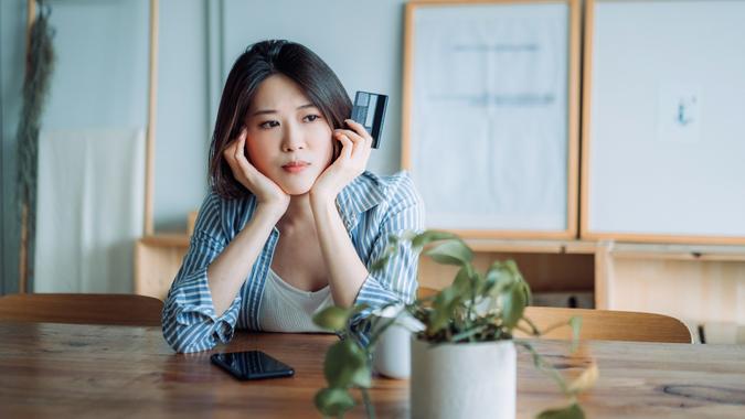 Young asian woman having trouble with her credit card and looking worried.  Financial problems, banking, finance, credit card fraud stock photo