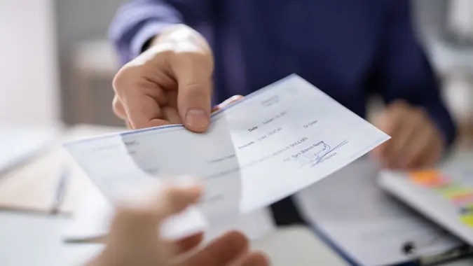 Businessperson Hands Giving Cheque To Other Person.