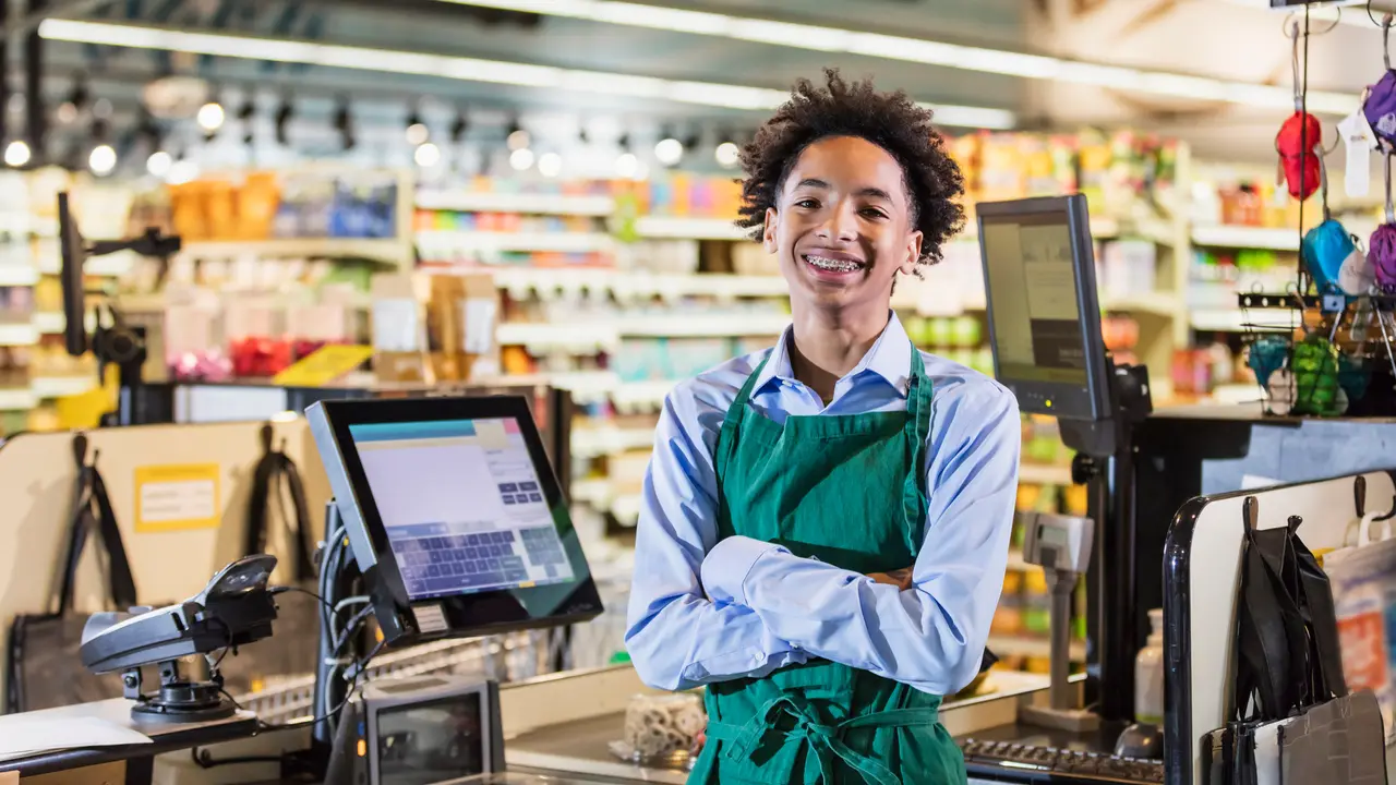 A mixed race African-American and Hispanic teenage boy working in a supermarket at the checkout counter.