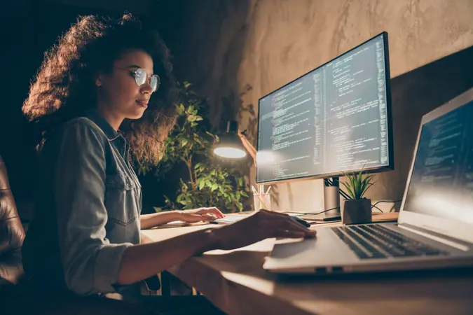 Profile side photo of concentrated skilled web expert afro american girl sit evening, desk use computer netbook work java script html back-end algorithm in workstation workplace.