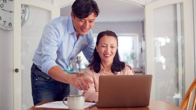 Mature Asian couple at home using laptop to organize household bills and finances.