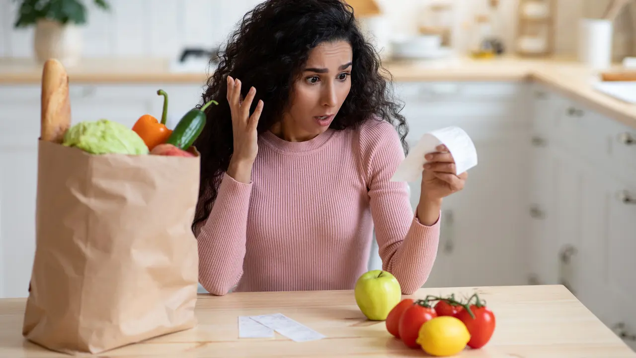 Portrait Of Shocked Young Housewife Checking Grocery Bills In Kitchen After Food Shopping In Supermarket, Millennial Lady Frustrated About Expensive Prices For Organic Products, Free Space.