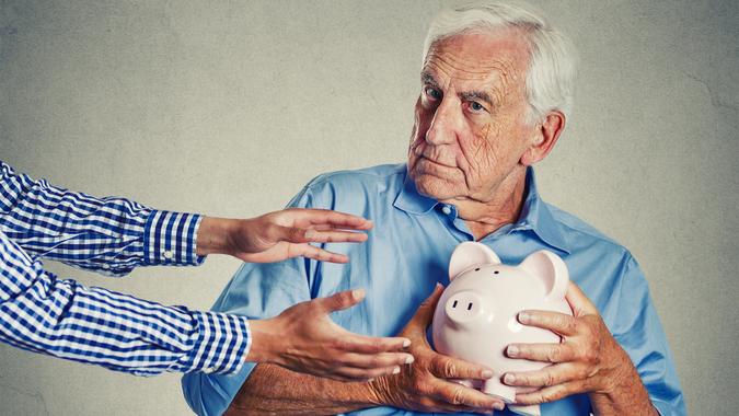 Closeup portrait senior man grandfather holding piggy bank looking suspicious trying to protect his savings from being stolen isolated on gray wall background.