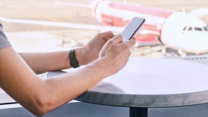 Man on mobile phone waiting for his flight at airport. Male hands holding smartphone stock photo