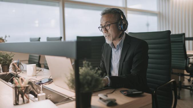 Asian chinese mature businessman with beard typing and replying email to his customer and video call with his client in the office using laptop stock photo