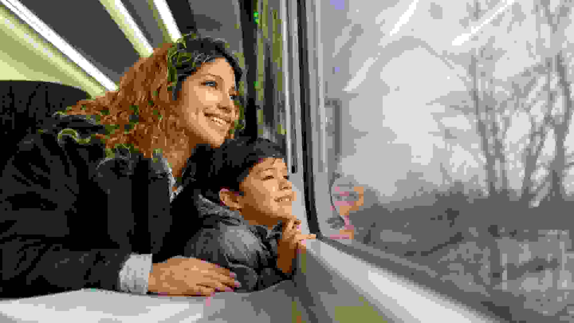 Happy single mother and son looking at the window view both smiling while traveling by train - Lifestyles .