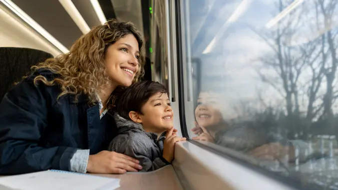 Happy single mother and son looking at the window view both smiling while traveling by train - Lifestyles .