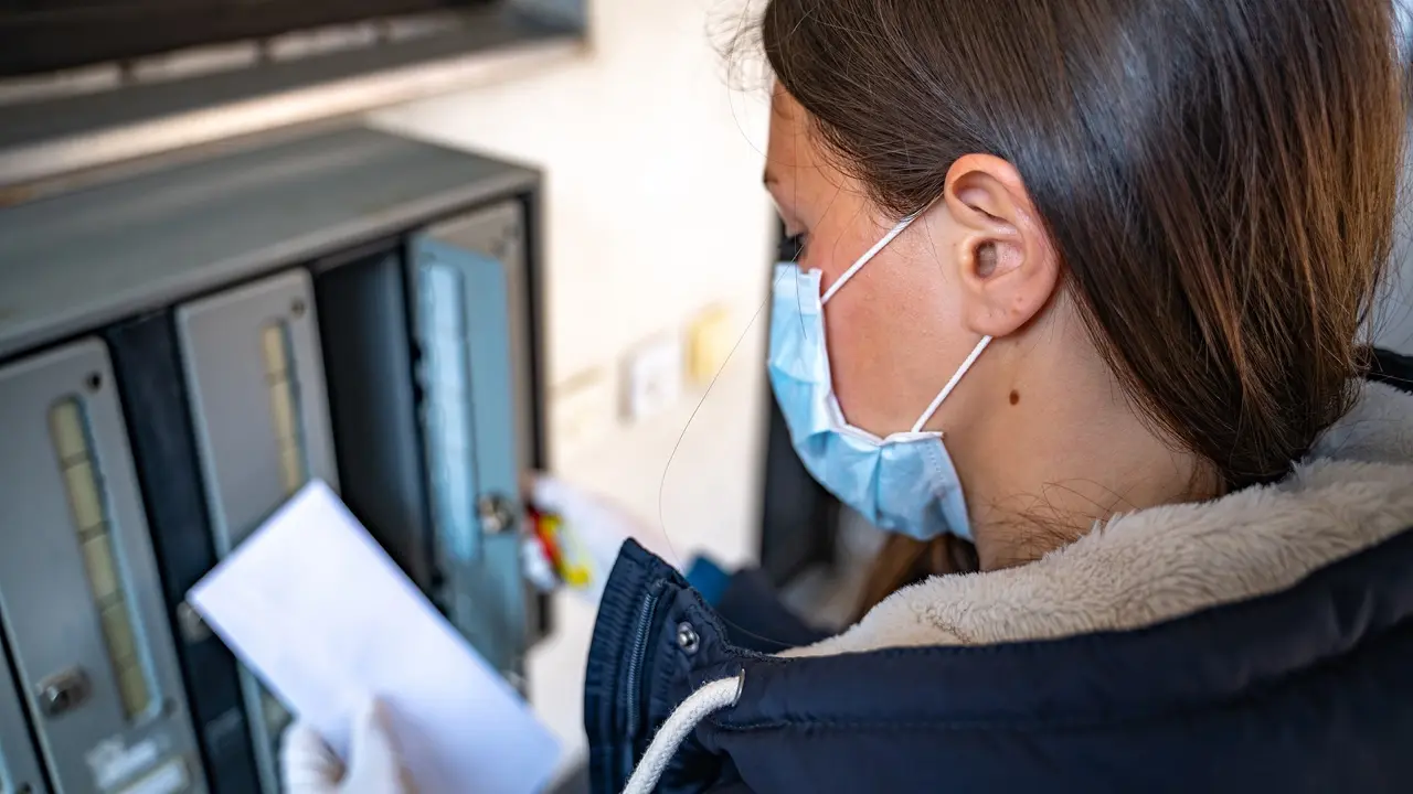 Rear View of Woman Getting Bills from Mailbox Wearing Surgical Mask During the Trying Times of Coronavirus Pandemic - stock photo stock photo