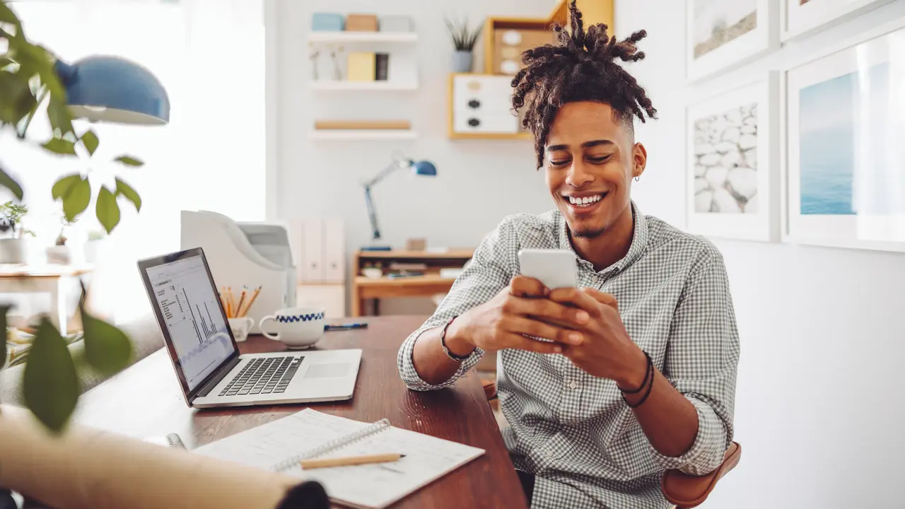 Picture of a young man sitting and using mobile device at his home to check his bank account balances
