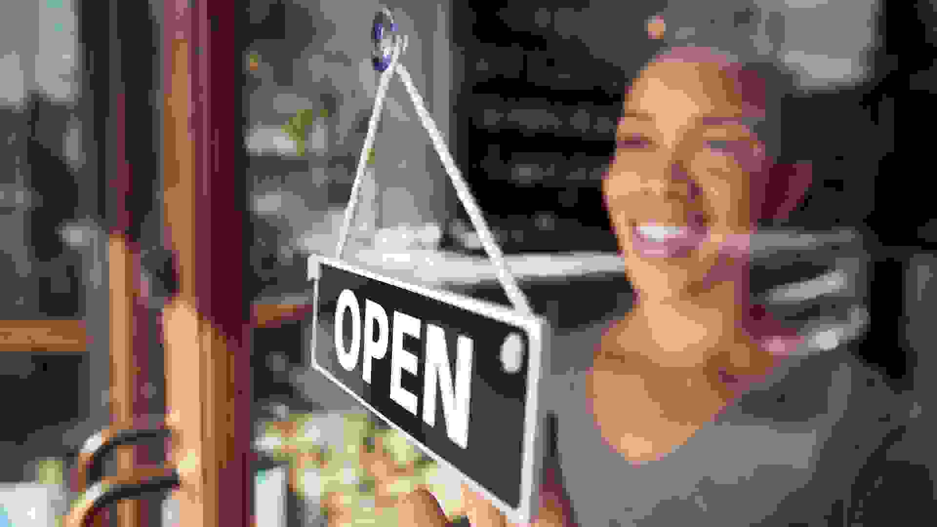 Female Owner Of Start Up Coffee Shop Or Restaurant Turning Round Open Sign On Door.