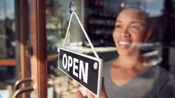 Female Owner Of Start Up Coffee Shop Or Restaurant Turning Round Open Sign On Door.