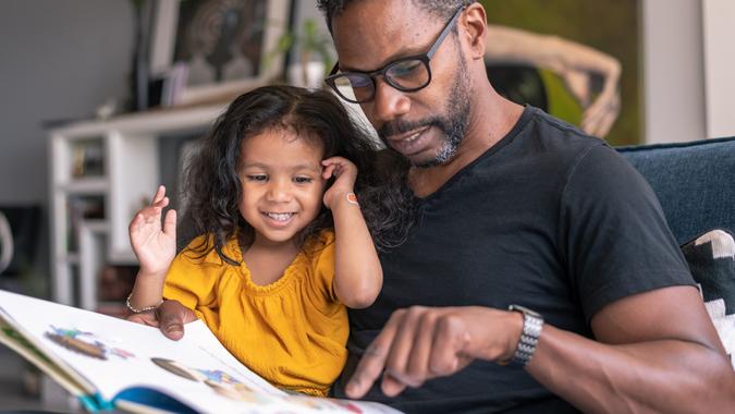 Affectionate father reading book with adorable mixed race daughter stock photo