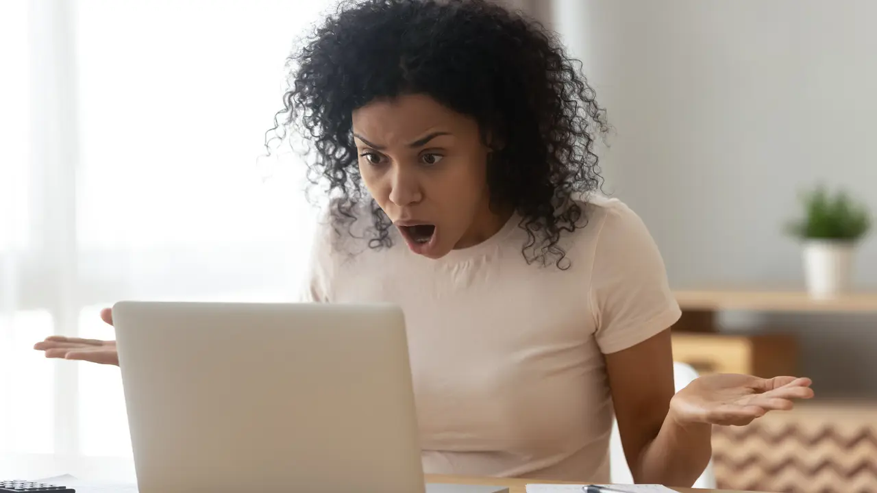 Shocked angry stressed african black woman customer looking at laptop screen feel bad surprise annoyed reading online news frustrated with stuck computer problem website error sit at home office desk.