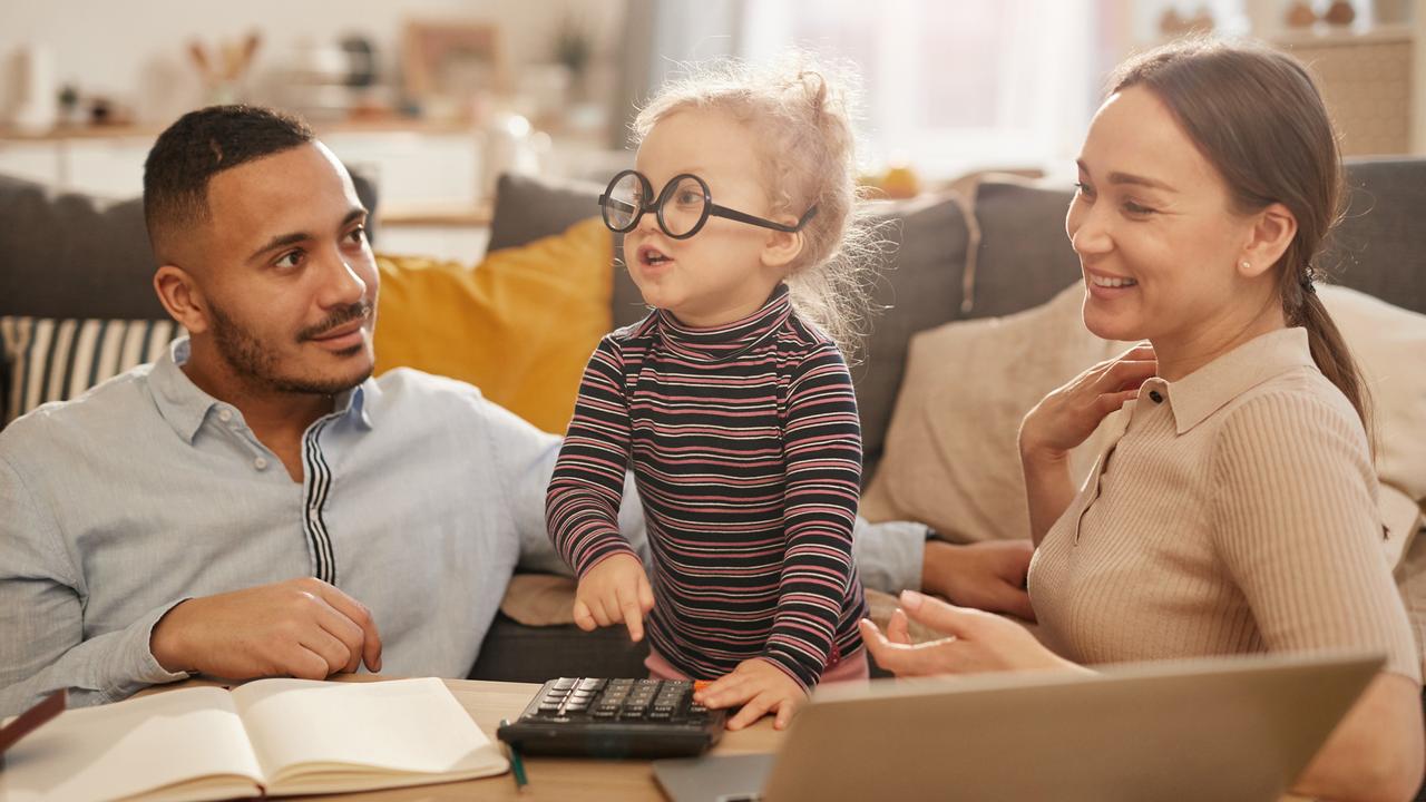 Portrait of happy young family counting home finances with cute little girl wearing glasses in sunlit apartment.