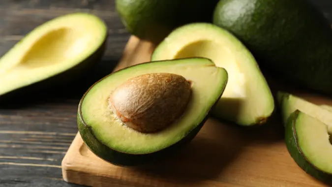 Board with avocado on wooden background, close up.