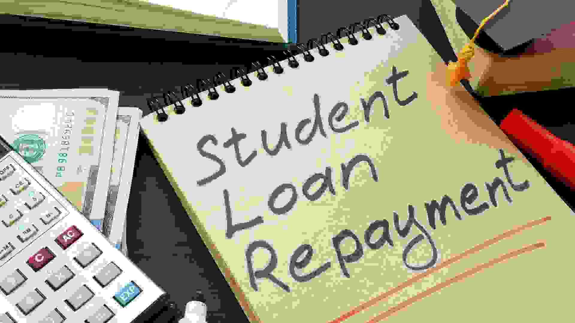 Student loan repayment sign, notepads, calculator and cash.