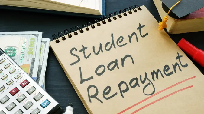 Student loan repayment sign, notepads, calculator and cash.
