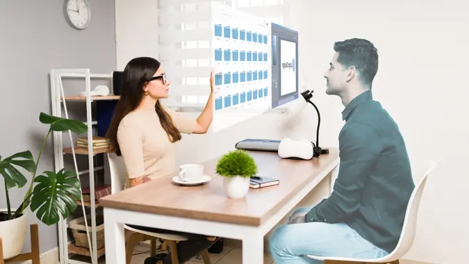 Smart young woman talking with a virtual man in the metaverse at her office using augmented reality glasses.