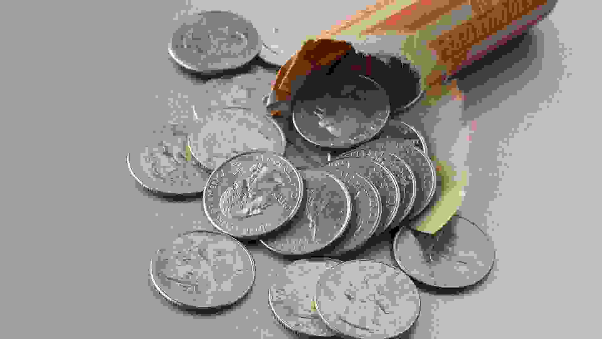 Brightly lit image of circulated US quarter dollar coins and paper roll on steel surface.