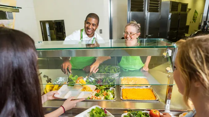 Friendly cafeteria workers serving healthy food to high school students.