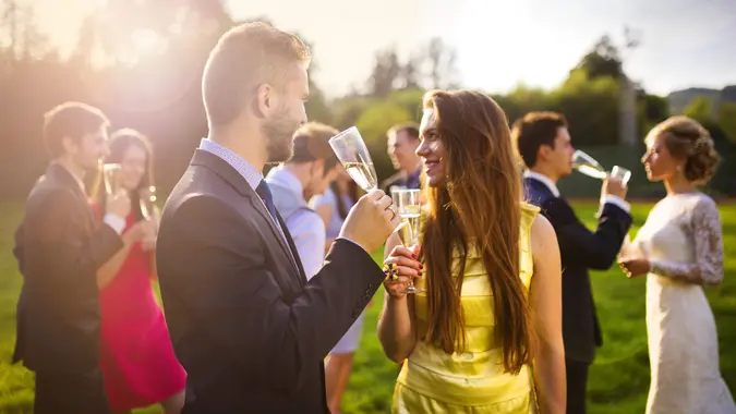 Wedding guests clinking glasses while the newlyweds drinking champagne in the background.