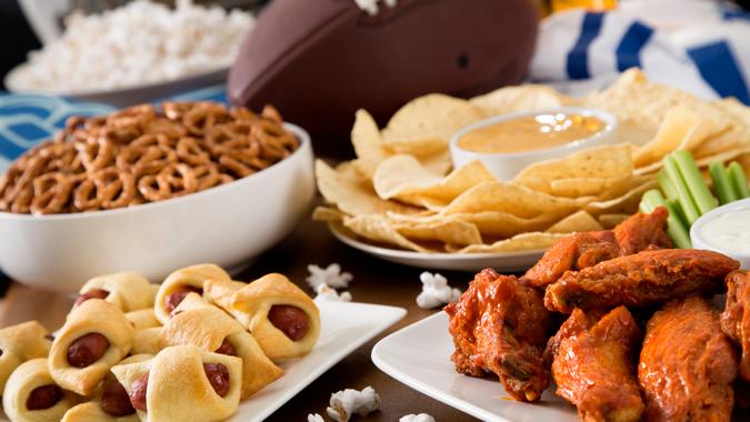 Hot wings, nachos, pigs in a blanket, beer, and popcorn, a tailgate party spread.