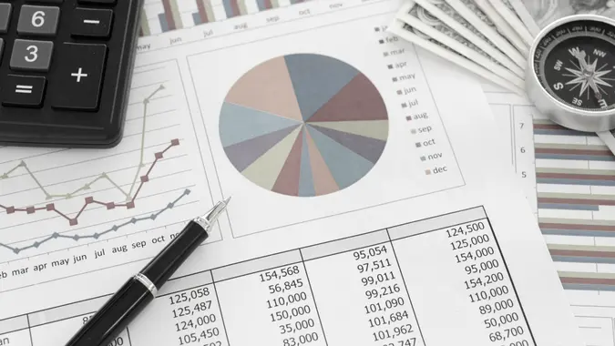 Pen on Pie chart and graphs business report with money, compass, calculator on desk of financial advisor.
