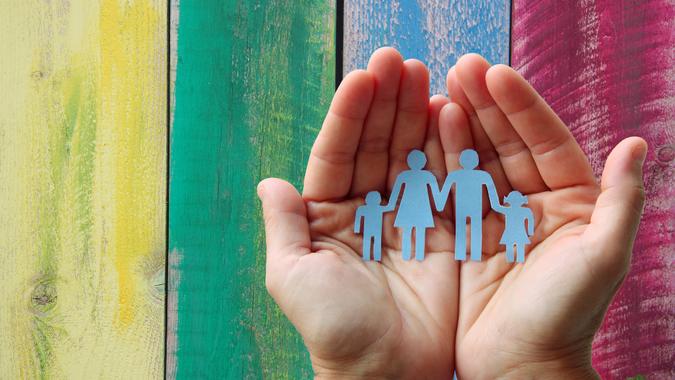Paper family in hands on wooden coloured background welfare concept.