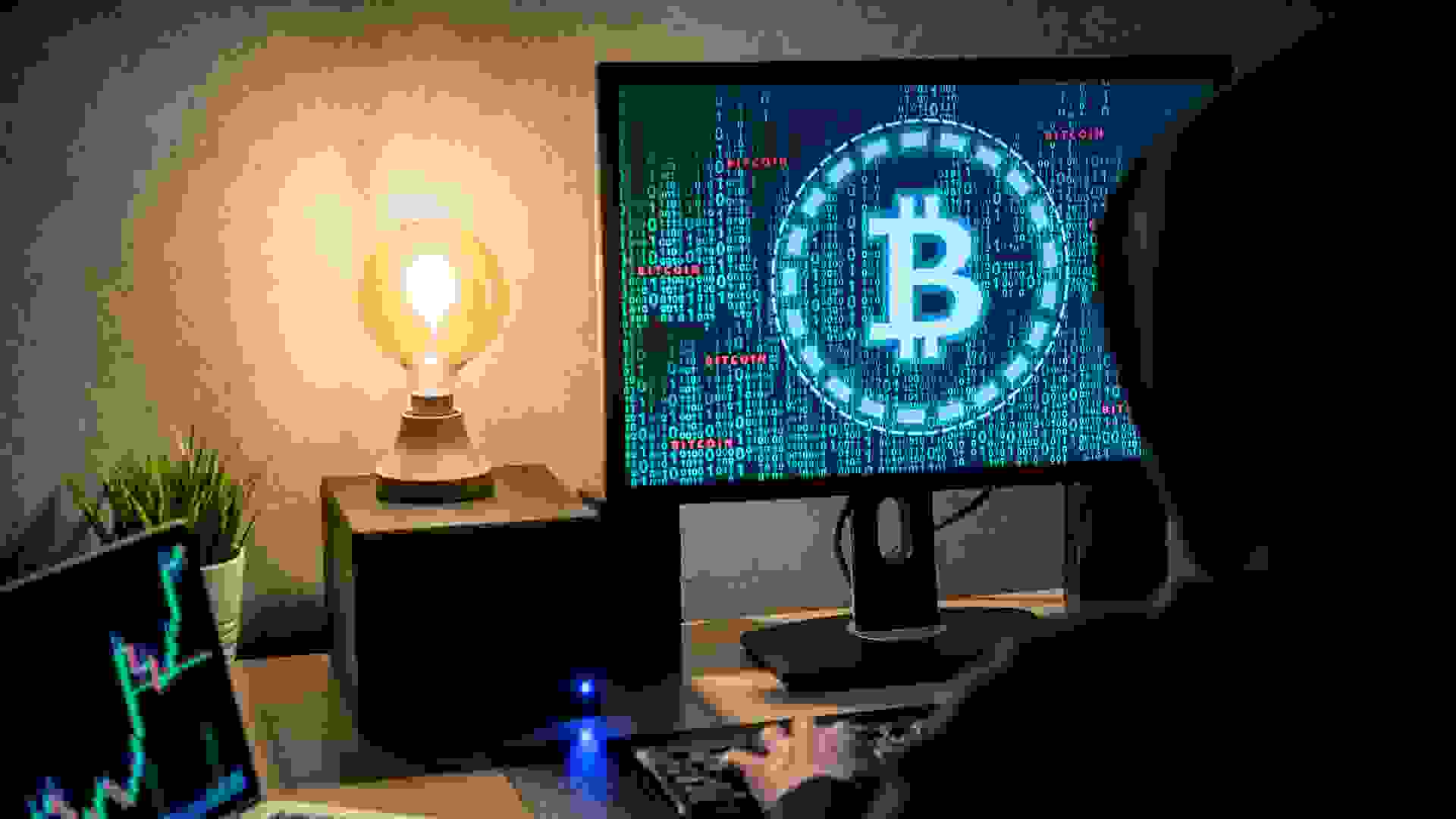 Hacker man using laptop and computer with green binary graphic and cryptocurrency candlestick graph price on monitor screen.