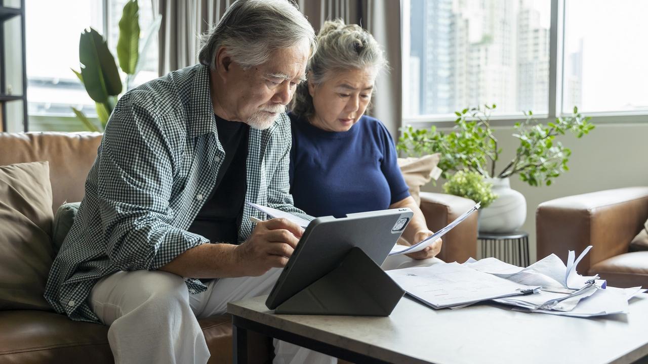 Old retired asian senior couple checking and calculate financial billing together on sofa involved in financial paperwork, paying taxes online using e-banking laptop at living room home background stock photo
