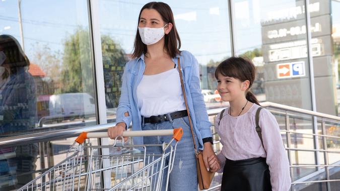 Mom in mask holding her daughter hand and standing together outdoors near the supermarket, shopping day. stock photo