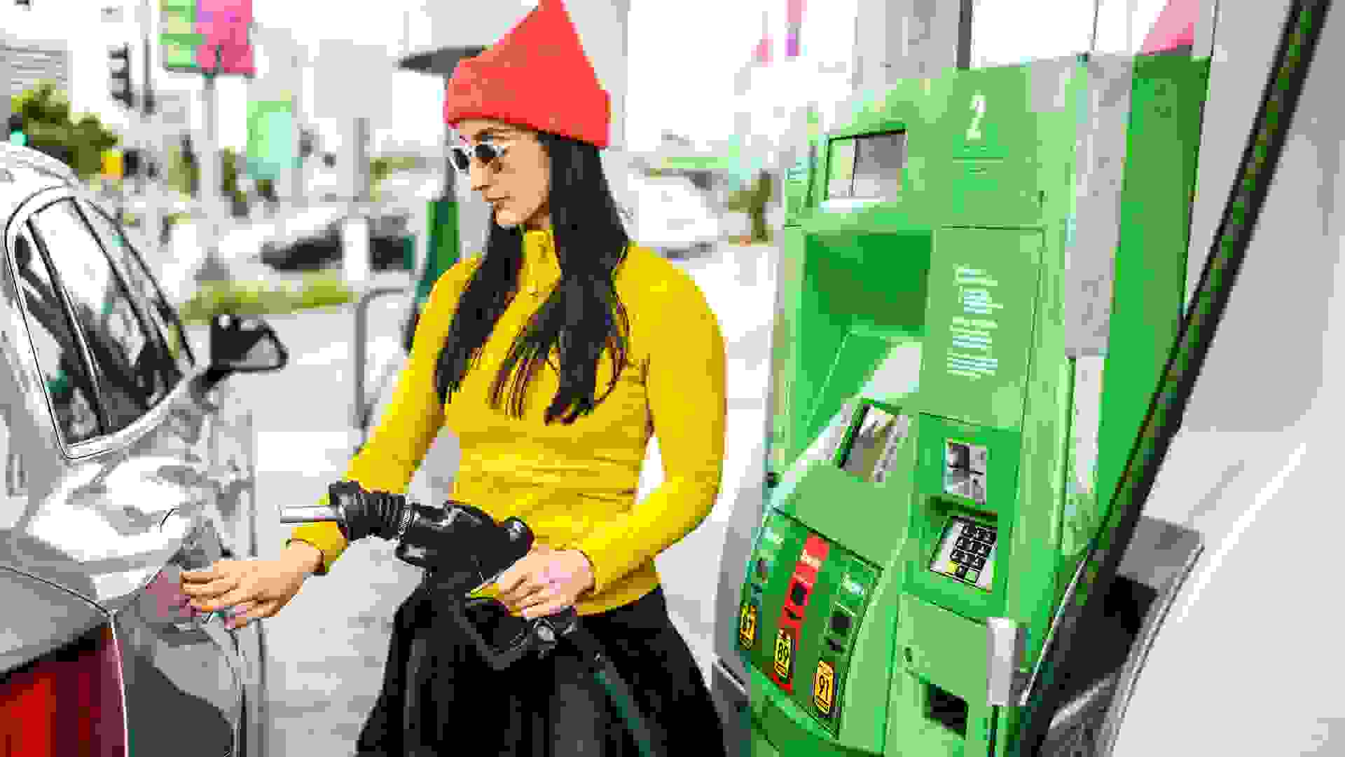 A woman inserting a gas pump nozzle at a gas station stock photo