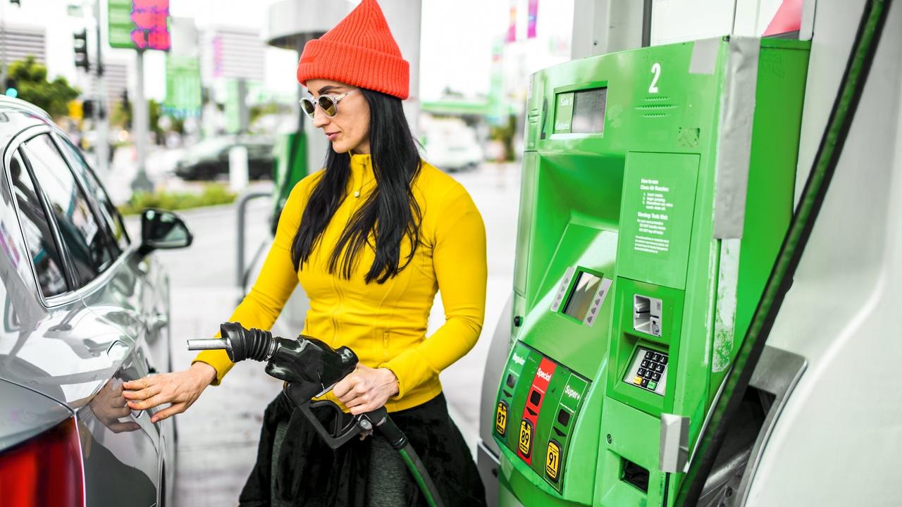 A woman inserting a gas pump nozzle at a gas station stock photo
