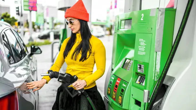 Une femme insérant une buse de pompe à essence dans une station-service photo stock