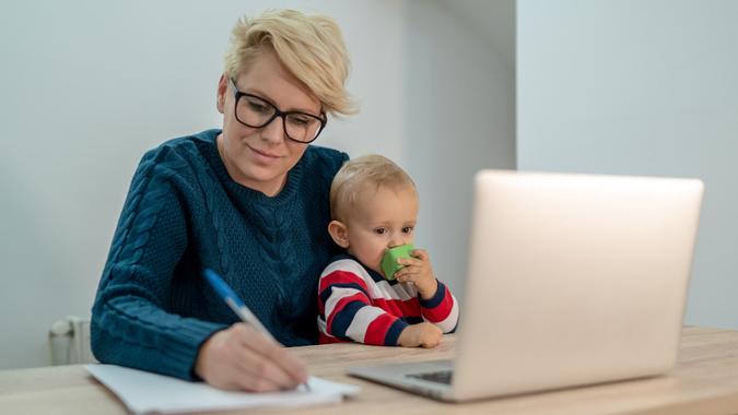 Young mother sitting at the table with her baby son on her lap, using a laptop. stock photo
