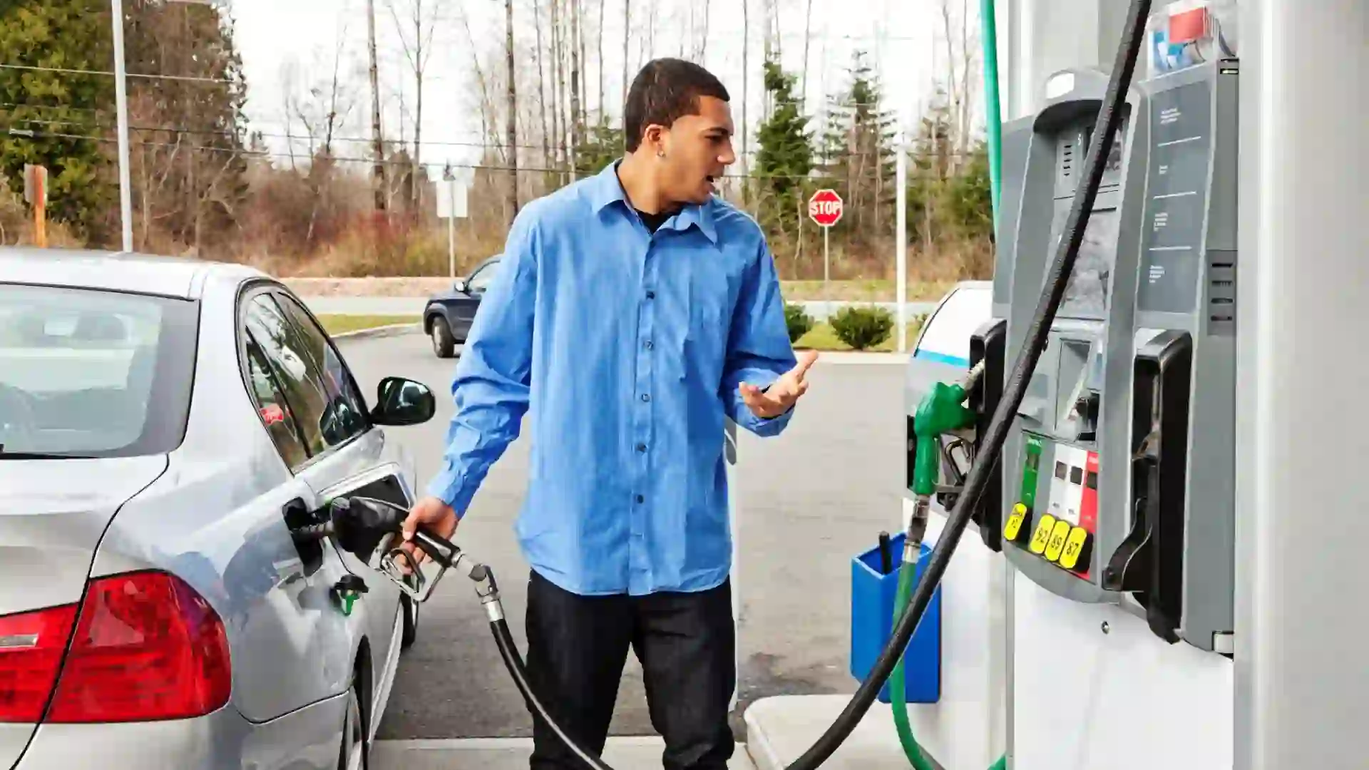 "Photo of a young man watching filling his gas tank, watching in disbelief as the dollar amount climbs on the gas pump display too quickly to comprehend.