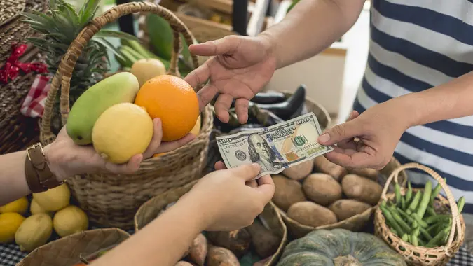 A man hands over a 100 dollar bill to a vendor pay for a few fruits. A purchase at a small market stall. stock photo