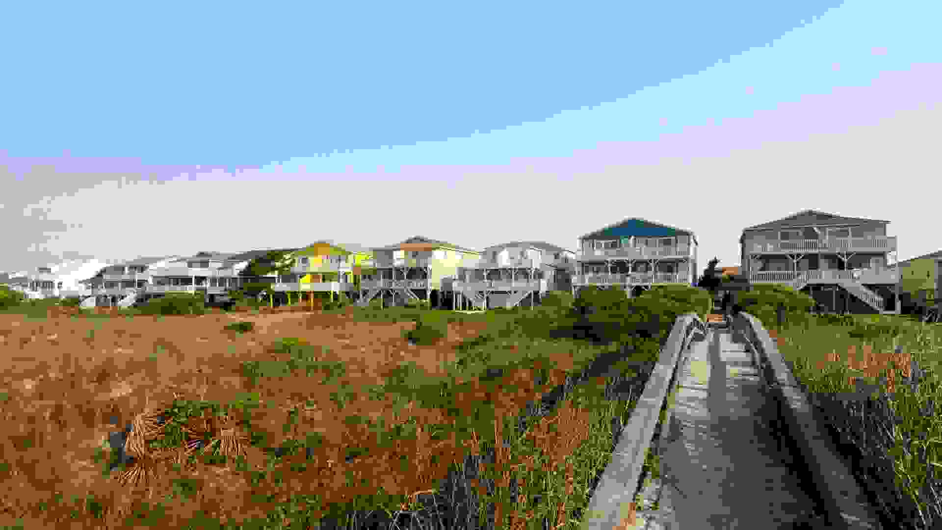 Beach houses across the green sand dunes with a long wooden walkway, Sunset Beach, North Carolina.