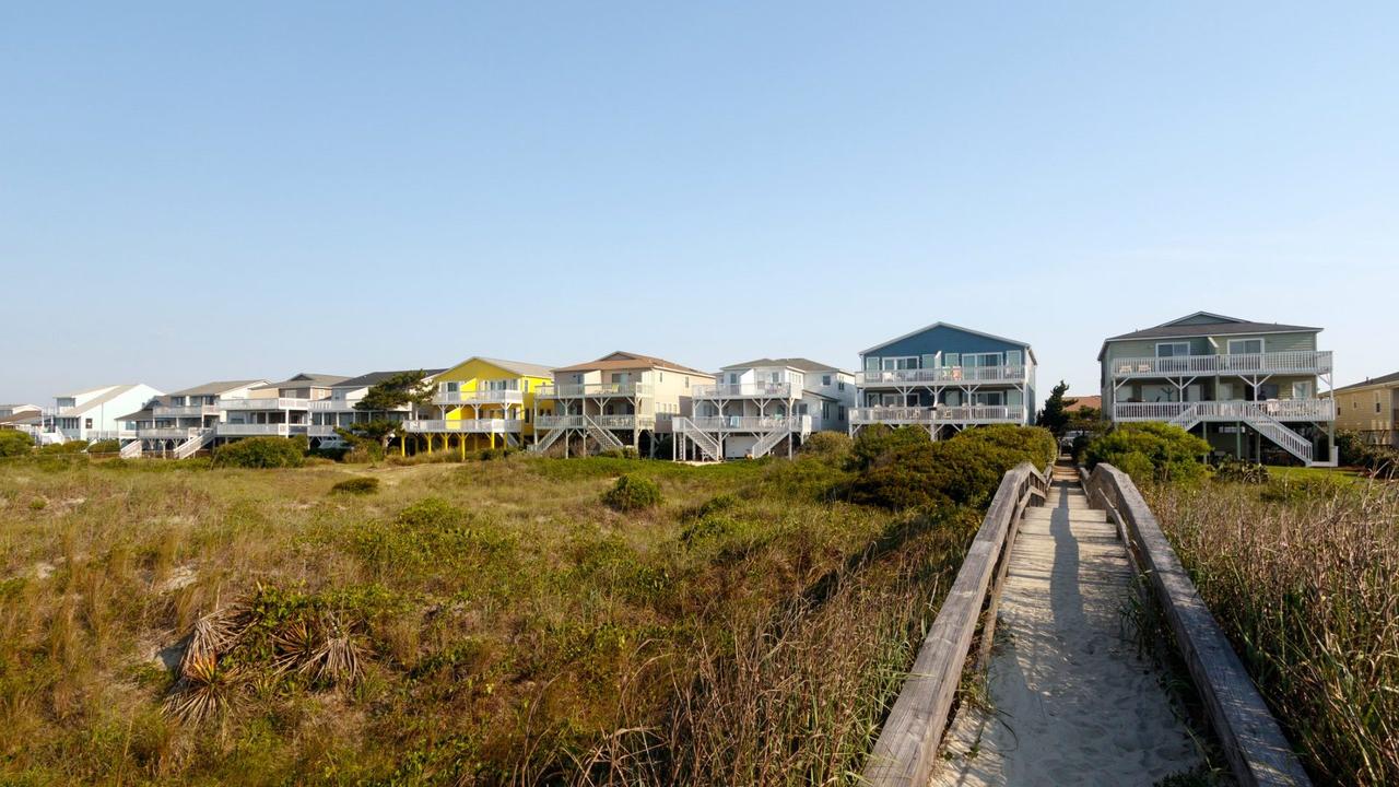 Beach houses across the green sand dunes with a long wooden walkway, Sunset Beach, North Carolina.