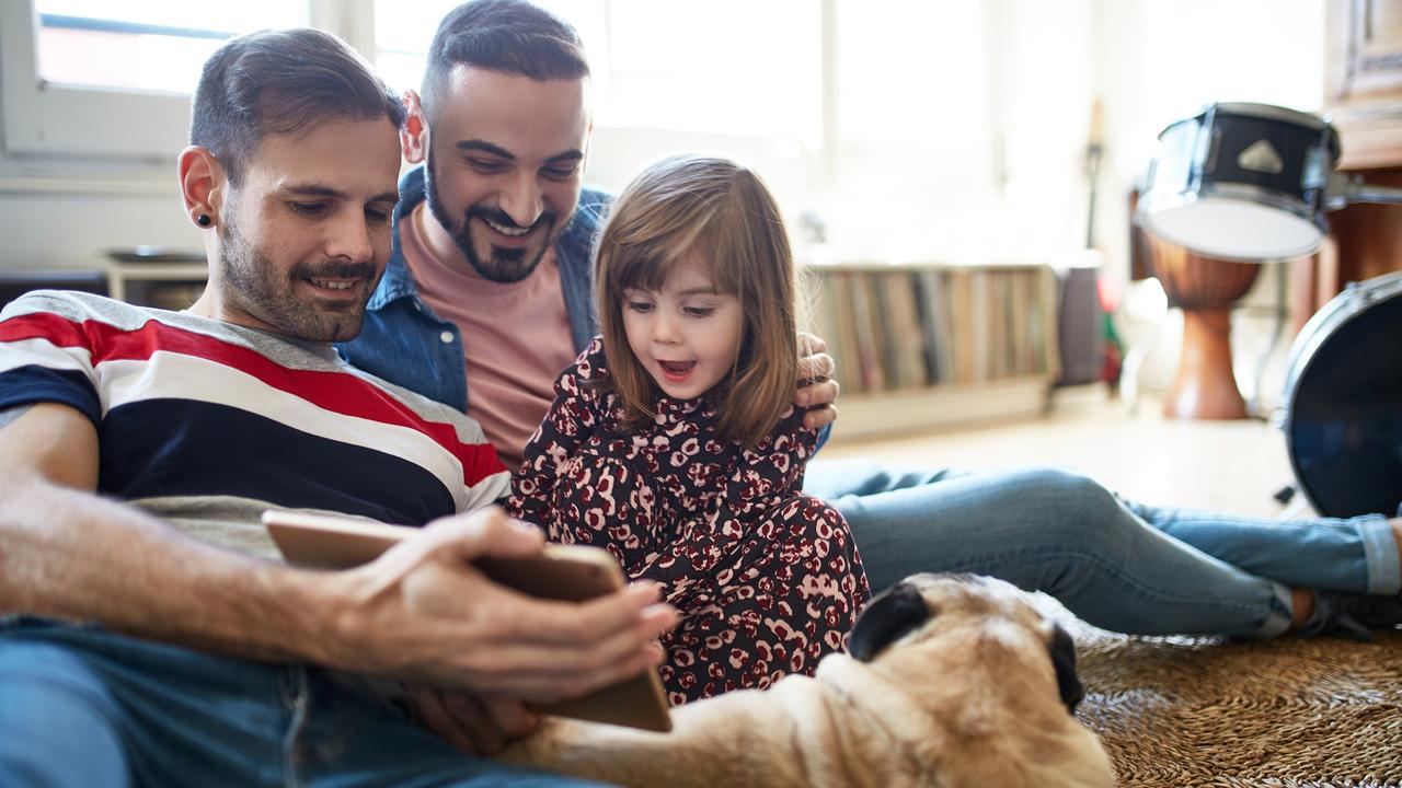 Smiling Spanish fathers enjoying weekend leisure with young daughter and dog as they use digital tablet together on living room floor.