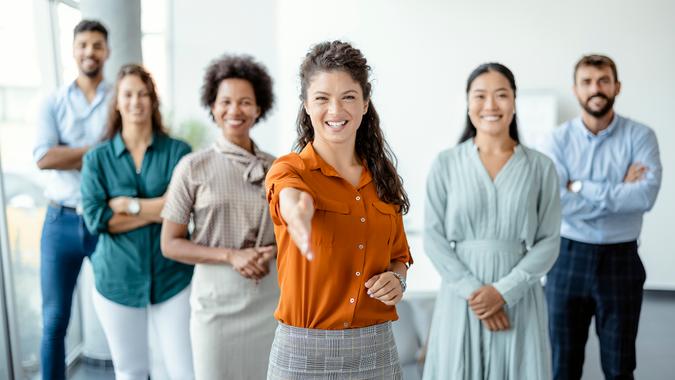 Head shot portrait smiling businesswoman offering handshake, standing with extended hand in modern office, friendly hr manager or team leader greeting or welcoming new worker.