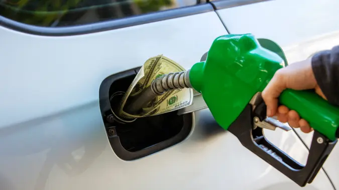 Conceptual photo showing inflation and economic impact at the gas pump with hundred dollar bills inside the tank.