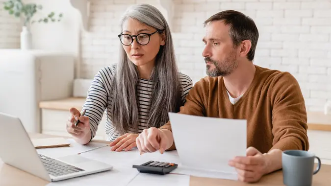 Mature middle-aged couple family wife and husband counting funds, savings declarations, investments,paperwork, financial documents, bankruptcy, court case, bills, pension with laptop. stock photo